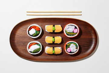 Set of paper sushi on a wooden plate over white background. Top view with copy space. Pure and fresh concept and composition.