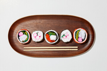 Set of paper sushi on a wooden plate over white background. Top view with copy space. Pure and fresh concept and composition.