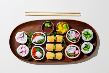 Set of paper sushi on a wooden plate over white background. Top view with copy space. Pure and fresh concept and composition.