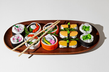 Set of paper sushi on a wooden plate over white background. Top view with copy space. Pure and fresh concept and composition.
