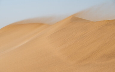 Strong wind blowing sand across the textured surface of the dunes in the rugged Namib Desert landscape
