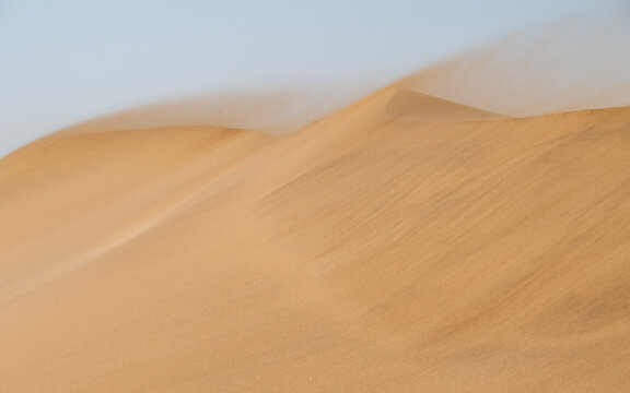 Strong wind blowing sand across the textured surface of the dunes in the rugged Namib Desert landscape