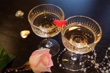Romantic Valentine's Day still life with champagne glasses, pink rose, candles and red heart on dark background
