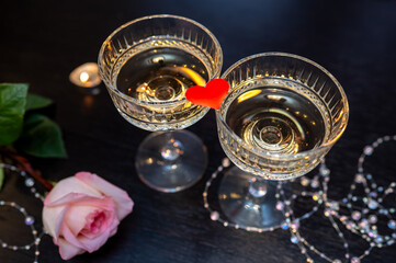 Romantic Valentine's Day still life with champagne glasses, pink rose, candles and red heart on dark background