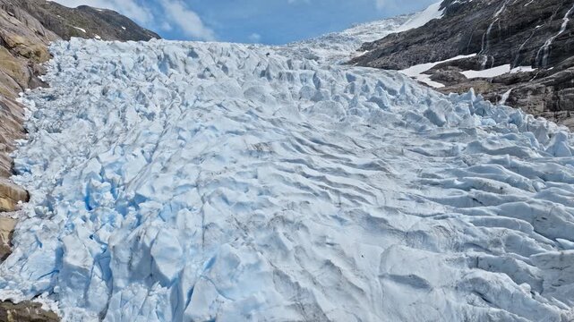 Aerial view over cracked ice surface of Briksdalsbreen glacier in Norway. Blue ridges and deep crevasses form dramatic natural patterns during summer conditions.