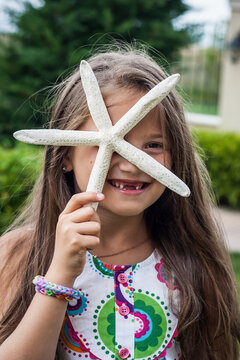 Portrait of a smiling girl with a missing tooth holding a starfish in front of her face