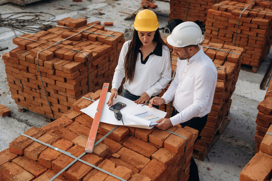 Discussing the plan, with documents. Female manager and male builder are on the construction site