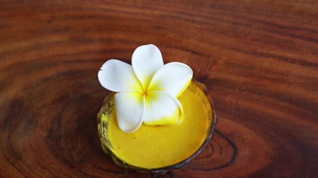 Organic ubtan facial in bowl close up on a wooden background. Champa flower petals and natural face mask cosmetic concept. Homemade natural skincare product for beauty treatment. Ayurvedic paste
