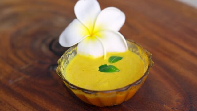 Organic ubtan facial in bowl close up on a wooden background. Champa flower petals and natural face mask cosmetic concept. Homemade natural skincare product for beauty treatment. Ayurvedic paste