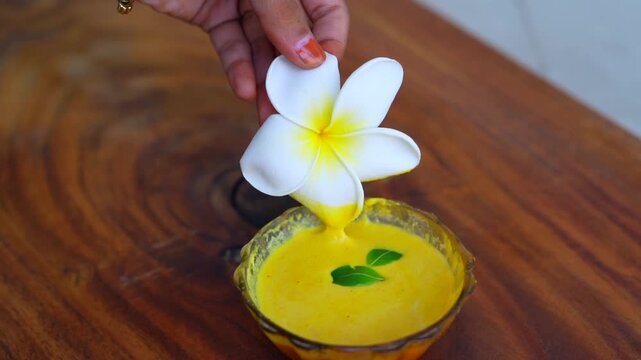 Organic ubtan facial in bowl close up on a wooden background. Champa flower petals and natural face mask cosmetic concept. Homemade natural skincare product for beauty treatment. Ayurvedic paste