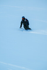Skier carving through powder on a blue winter day, off-piste adventure in fresh snow