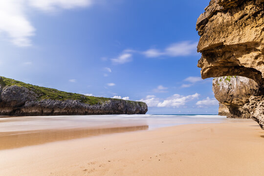 A deserted sandy Playa de Guadam&iacute;a during low tide on a sunny day, carved out of the rock by the Atlantic ocean. Playa de Guadam&iacute;a, Llanes, Asturias, Spain.