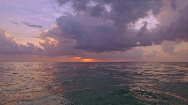 Camera emerging from underwater to open sea horizon at sunset, water surface breaking in foreground with dramatic clouds and glowing sky, slow motion ocean atmosphere