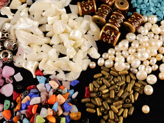 A variety of beads made of natural stone, glass, mother-of-pearl, ceramics and metal on a black background	
