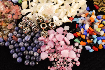 A variety of beads made of natural stone, glass, mother-of-pearl, ceramics and metal on a black background	