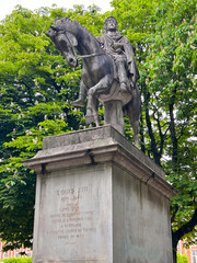 Equestrian marble statue of King Louis XIII surrounded by green crowns of chestnut trees in the park of Place des Vosges.