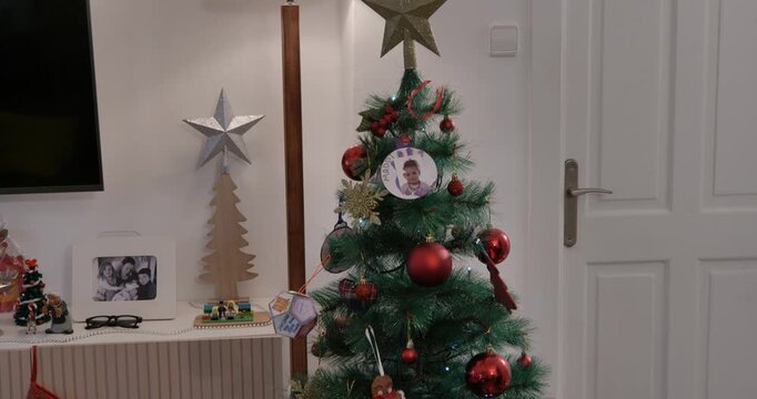 Tilt-down shot of a Christmas tree decorated with red baubles and family photos, revealing the traditional Basque Olentzero figure at the base.