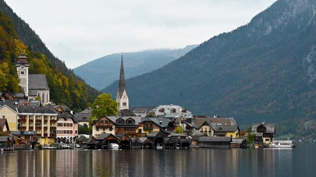 Hallstatt, Austria -  October 12, 2025: Sensic view of Hallstatt village with traditional alpine houses, church tower and mountains reflected in the lake. Scenic autumn landscape in Austria, popular t