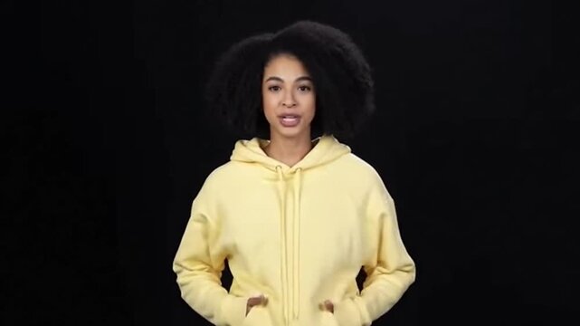 Young woman wearing yellow hoodie holding drawstring against black background