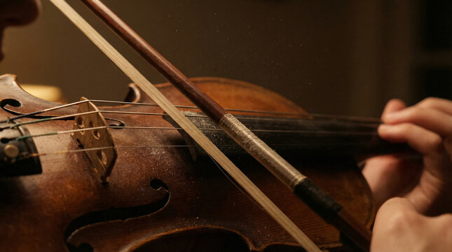 a violin bow drawing across strings in dim lamplight