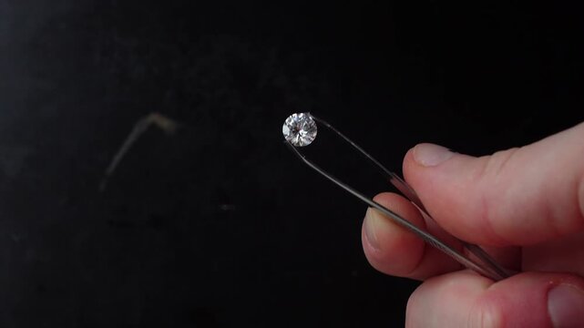 Close-up of a faceted gemstone held with tweezers against a dark background