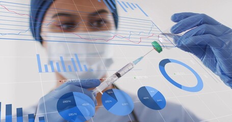 Nurse preparing syringe in lab wearing surgical cap, mask, blue gloves, holding vial, data charts