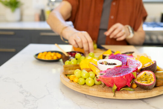 Colorful dragon fruit and grapes are resting on round wooden serving board on marble countertop