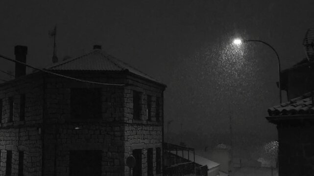 Heavy snow falls on a silent residential street in &Aacute;vila at night, covering pavements and trees, while soft street lighting adds a peaceful, wintry atmosphere to the urban landscape.