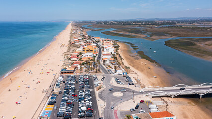 Aerial view of Praia de Faro showing the sandy beach, surrounding buildings, river, and parked...