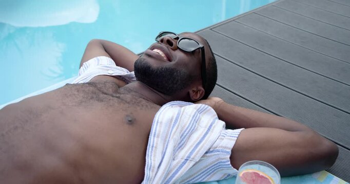 Camera is zooming while sunlight is reflecting on pool water, highlighting sunglasses on towel