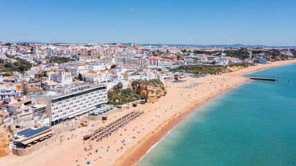 Fototapeta premium Visitors relax on the sandy beach of Albufeira while others swim in the water during a sunny day, revealing the town's vibrant waterfront and marina