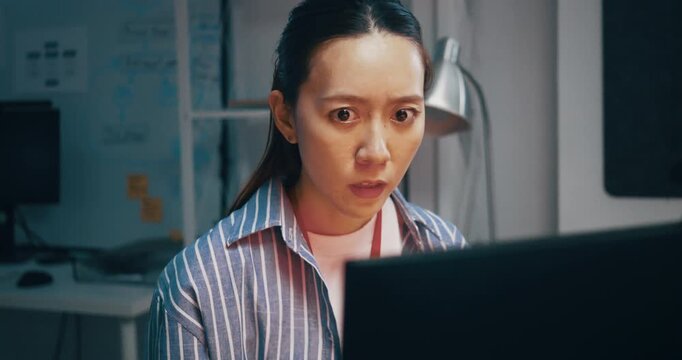 Shocked woman staring at her computer screen with a surprised expression in a dark office.	
