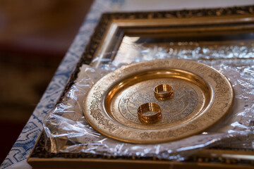 Golden Wedding Rings Resting on Ornate Religious Plate in Church Setting with Rich Textures and Warm Lighting