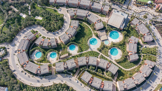 Aerial view of a residential area in Albufeira, Portugal, featuring multiple buildings and circular swimming pools surrounded by trees