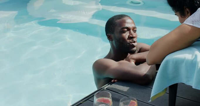 Couple on sunny day sparking conversation with man at pool edge leaning, woman bracing by drinks