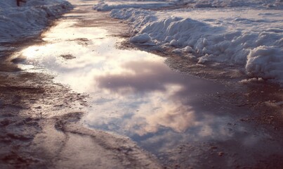 A puddle of water on the ground with a reflection of the sky