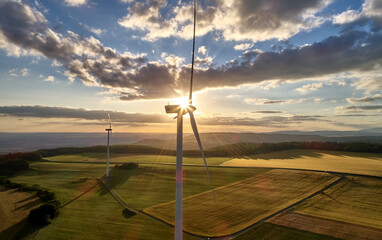 Wind turbines producing renewable electricity at sunset above agricultural landscape. Ideal for: clean energy, sustainability, energy transition, smart grid, decarbonization concepts. 