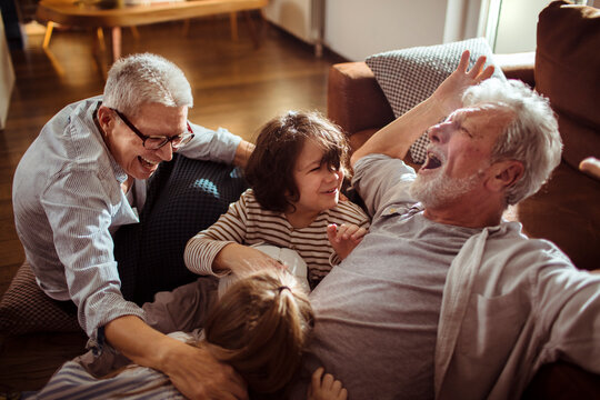 Grandparents playing and laughing with grandchildren at home in living room