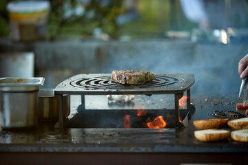 Beef steak grilling over open fire on barbecue grill with flames and smoke. Ideal for: food advertising, barbecue marketing, restaurant promotion, outdoor cooking, premium meat concepts.