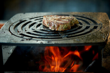 Beef steak grilling over open fire on barbecue grill with flames and smoke. Ideal for: food advertising, barbecue marketing, restaurant promotion, outdoor cooking, premium meat concepts.