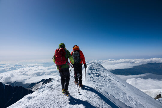 Two climbers on the Mont Blanc summit ridge descending under clear blue sky