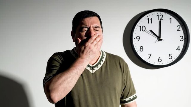 Man yawning in front of a wall clock showing 10 oclock