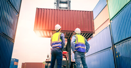 Two Engineer or foreman wears PPE checking container storage with cargo container background at sunset. Logistics global import or export shipping industrial concept. © nuttawutnuy
