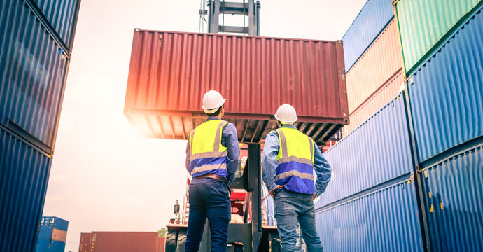 Two Engineer or foreman wears PPE checking container storage with cargo container background at sunset. Logistics global import or export shipping industrial concept.