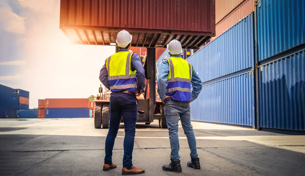 Two Engineer or foreman wears PPE checking container storage with cargo container background at sunset. Logistics global import or export shipping industrial concept.