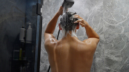 Man washing hair in modern bathroom shower with water spray