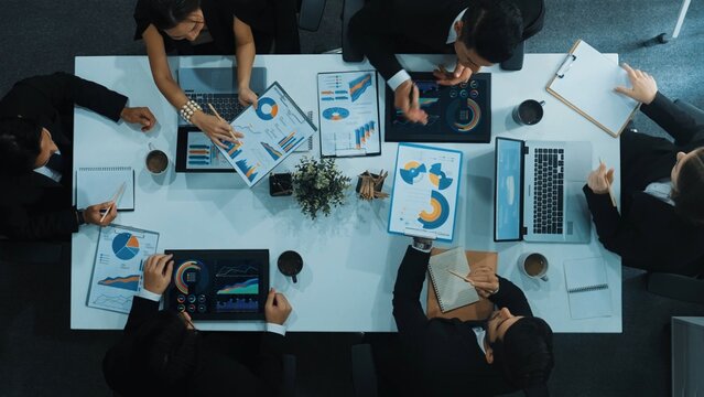 Top down aerial view of business people discussing about financial strategy on table with document and tablet display investment statistic at meeting. Diverse team brainstorm about plan. Directorate.