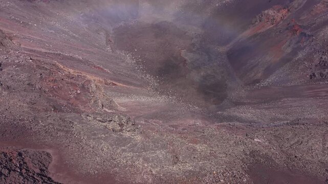 Drone footage ascending over the interior of a volcanic crater at Piton de la Fournaise on Reunion Island. Low clouds and mist move across the mineral landscape.