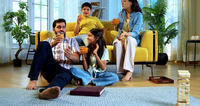 Indian family together drinks cold drink in glass as mother serves refreshing beverages to husband and kids while everyone enjoys happy bonding time indoors in modern lavish home