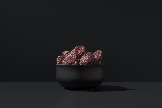Medjool dates in black bowl on dark background